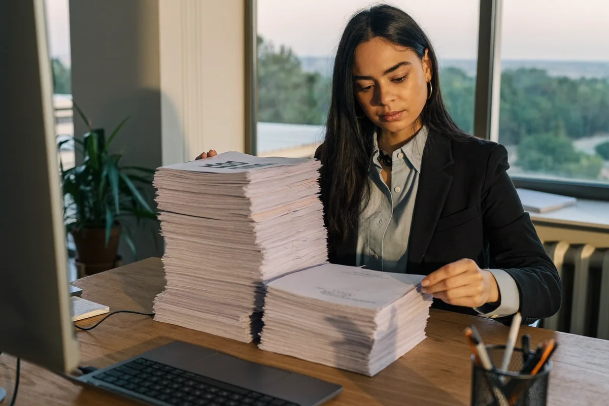 Profesional analizando contratos y documentos extensos junto a su laptop